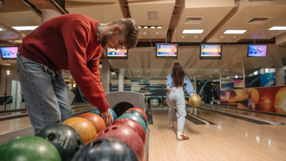 Joueur choisissant une boule de bowling pendant qu'une joueuse lance sur la piste