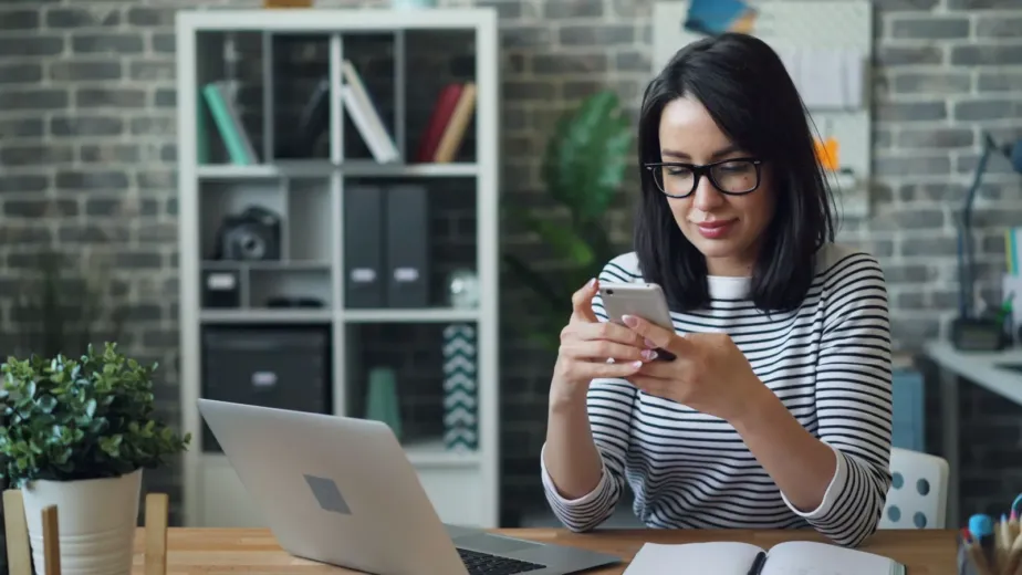 Femme réservant une activité sur son smartphone devant son ordinateur